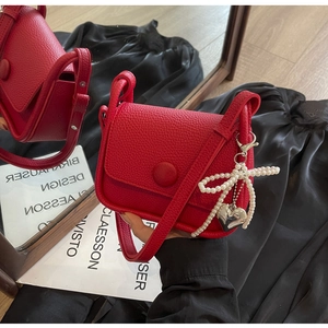 Close-up of red lychee leather saddle bag with pearl bow and silver heart charm