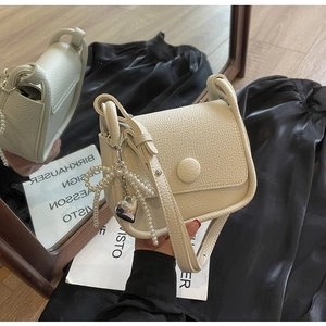 Detail of lychee textured saddle bag with pearl heart pendant and circular buckle
