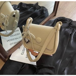 Detail of cream lychee leather saddle bag with pearl bow and metal heart charms