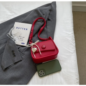 Detail of red saddle bag with lychee texture, pearl bow, and heart charm on grey suit