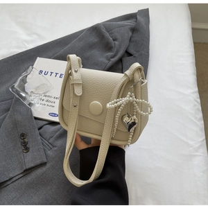 Detail of beige lychee leather saddle bag with heart pearl charm on a grey blazer