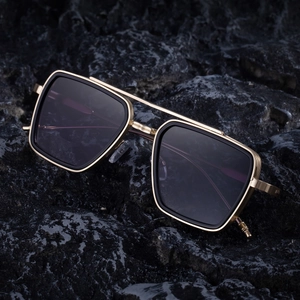 Men's square metal sunglasses with gold frame and dark lenses on a black stone background