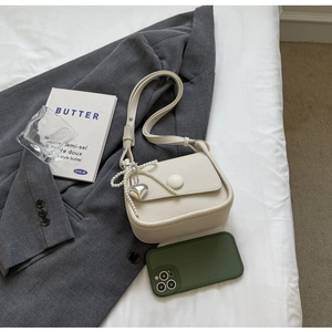 Detail of off-white lychee grain leather saddle bag with pearl heart charm and round buckle