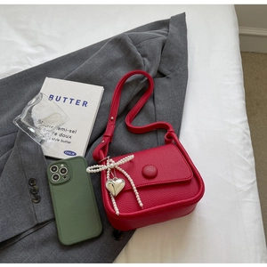 Detail of red lychee pattern saddle bag with pearl bow and heart pendant on white bedding