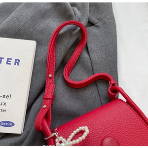Close-up of red lychee texture leather saddle bag with elegant pearl charm detail