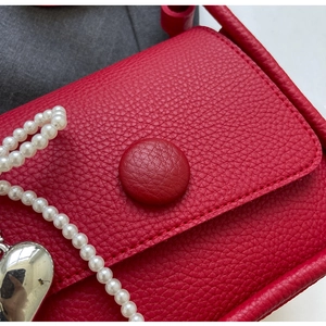 Detail of red lychee textured saddle bag with pearl strap and silver heart charm