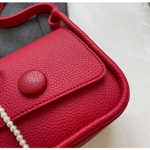 Detail of red lychee leather saddle bag with pearl chain strap and elegant clasp