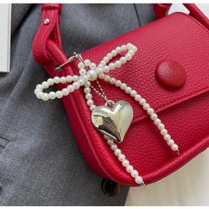 Detail of red lychee leather saddle bag with pearl bow and silver heart pendant