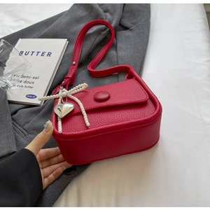Detail of red lychee grain leather saddle bag featuring pearl heart charm and round buckle