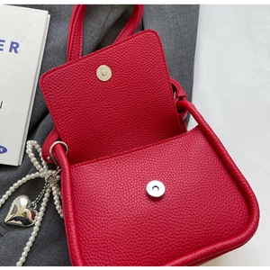 Detail of red lychee textured saddle bag with magnetic closure and pearl heart charm