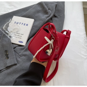 Close-up of red lychee leather saddle bag with pearl charms and heart-shaped pendant