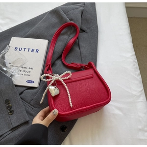 Detail of red litchi texture leather saddle bag with pearl bow and silver heart pendant