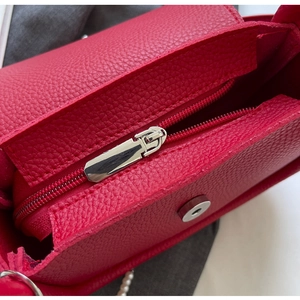 Detail view of red lychee leather saddle bag with silver zipper and pearl chain strap