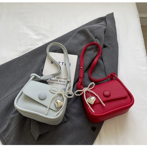 Close-up of pebble leather crossbody bags in blue and red with pearl bow and heart charm