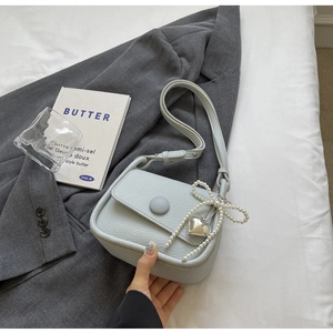 Close-up of light blue litchi grain saddle bag with pearl bow and heart charm