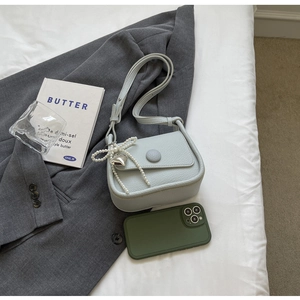 Detail of light blue lychee texture leather saddle bag with pearl bow and heart pendant
