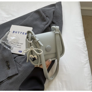 Close-up of light blue pebbled leather saddle bag with pearl bow and heart charm