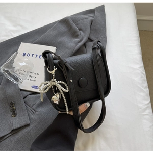 Close-up of litchi texture saddle bag with pearl bow and silver heart pendant on a blazer