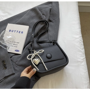 Detail of black litchi grain leather saddle bag with pearl bow and silver heart pendant
