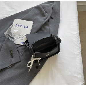 Detail of black lychee grain saddle bag with pearl bow charm on a grey suit jacket