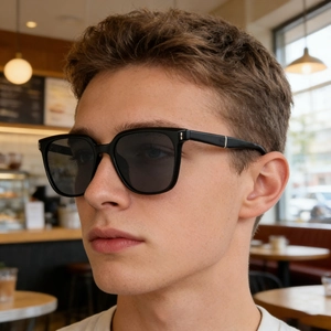 Male model wearing matte black square polarized sunglasses in a cozy cafe setting