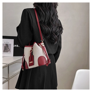 Detail of canvas bucket bag with burgundy leather trim and drawstring closure shown on model