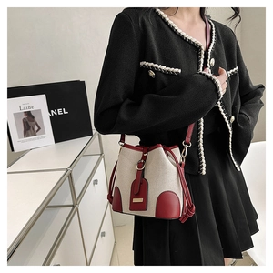 Detail of small beige canvas bucket bag with red leather trim and gold hardware