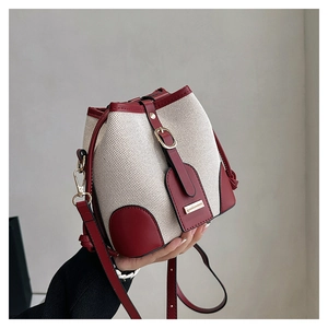 Detail of contrast stitching and red leather trim on the white bucket bag with metal buckle