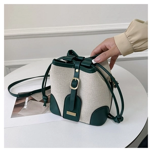 Detail of retro bucket bag featuring beige canvas and green leather trim with metal buckle