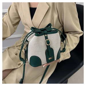 Detail of a beige canvas bucket bag with green leather trim and elegant gold metal hardware