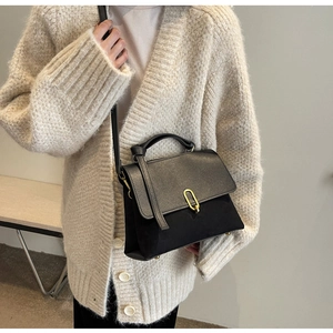 Detail of black tote bag featuring mixed textures and a gold-tone oval metal clasp