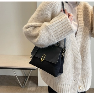 Close-up of a retro black crossbody bag featuring suede texture and gold horseshoe buckle