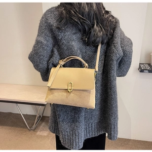 Detailed view of beige patchwork handbag with gold clasp worn over the shoulder