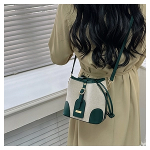 Detail of canvas bucket bag with green leather trim and gold buckle worn with a khaki dress