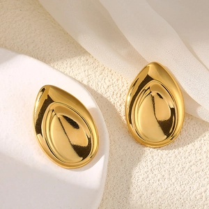 Detail of gold teardrop earrings with mirror finish on textured white stone background