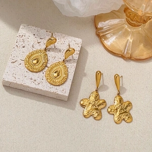 Detail of gold-plated waterdrop earrings and hammered star studs on stone surface