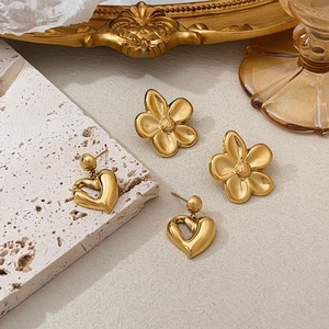 Detailed view of 18k gold heart and floral earrings displayed on elegant marble texture