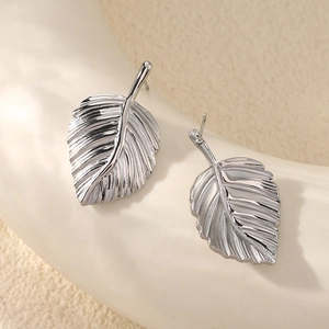 Vue macro de boucles d'oreilles feuilles argentées avec détails sur support beige