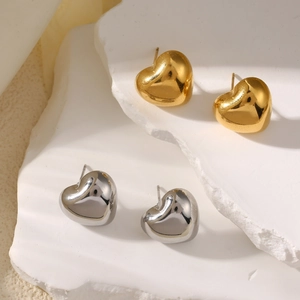Minimalist geometric heart stud earrings in gold and silver finish on a stone pedestal