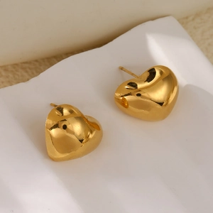 Detailed close-up of golden heart-shaped earrings on a white textured ceramic display tray