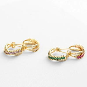 Detailed macro of gold C-shaped earrings with emerald-cut stones and micro-pave crystals