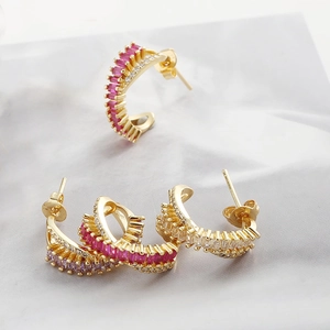 Detail of C-shaped gold earrings with emerald and amethyst zircons on marble