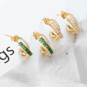 Close-up of gold C-shape stud earrings with emerald and white zircon pave setting
