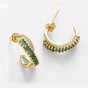 Detailed close-up of C-shaped gold earrings with emerald green stones and zircon accents