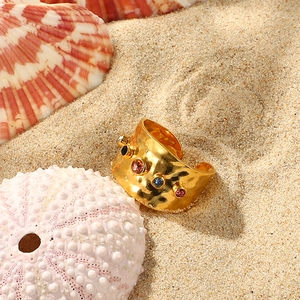 Hammered gold open ring with colorful gemstones on sand with seashells