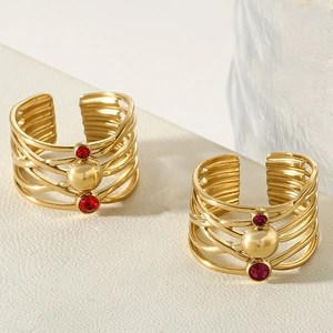 Macro detail of gold-plated braided ring featuring red crystal stones and central metal bead