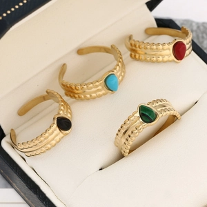 Detail of four teardrop rings with red, blue, green, and black stones in a velvet box