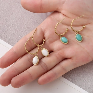 Gros plan de boucles d'oreilles créoles torsadées dorées avec pierres blanche et turquoise
