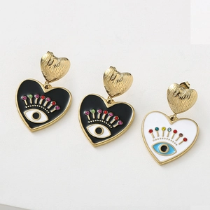 Détail de boucles d'oreilles cœur en métal brossé doré avec breloques œil en émail