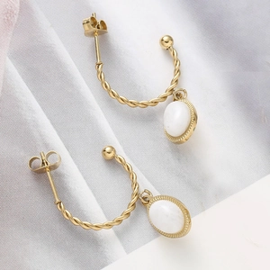 Détail de boucles d'oreilles torsadées dorées avec pendentifs ovales en marbre blanc